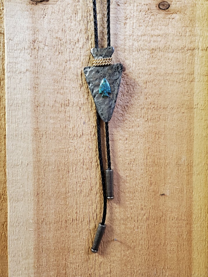 a large arrowhead bolo tie with a turqoise stone on a wooden background