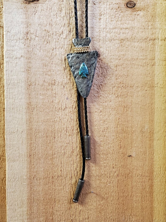 a large arrowhead bolo tie with a turqoise stone on a wooden background