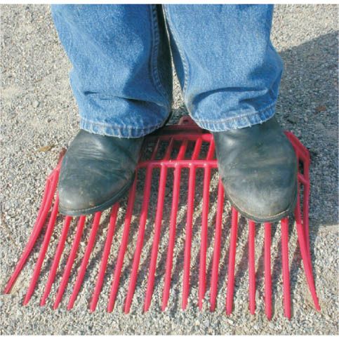 a man standing on a red plastic manure fork head designed for cleaning horse stalls, with a reinforced rounded plastic head and multiple prongs.